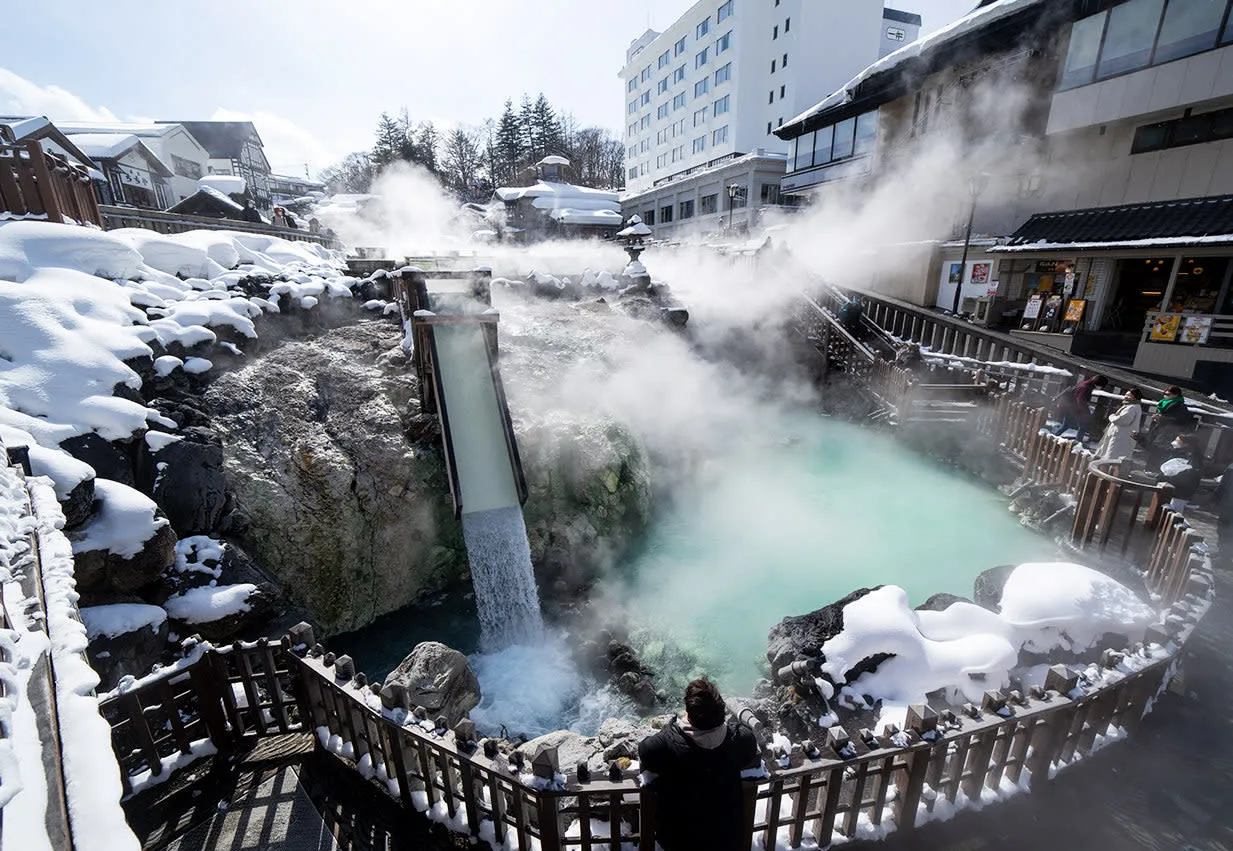 草津溫泉湯畑在雪中湧出白濁溫泉,蒸氣升騰、木造欄杆環繞,青綠泉水與皚皚白雪相映。