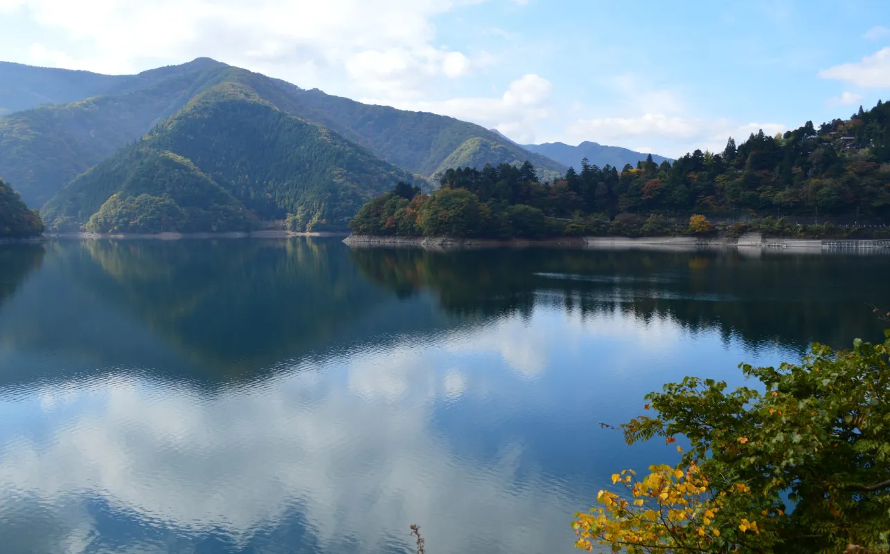 奧多摩湖碧綠湖面環繞蒼翠山巒,對岸森林與遠方山峰倒映水中,呈現東京都最深山的近郊湖景。