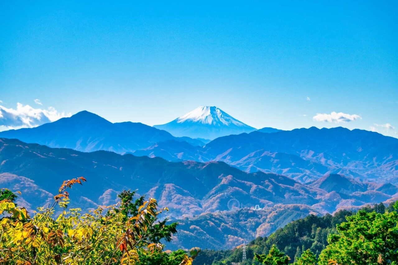 高尾山山頂區域,藍天白雲下群山連綿、樹林翠綠,可見遠方山脈起伏與天際線。