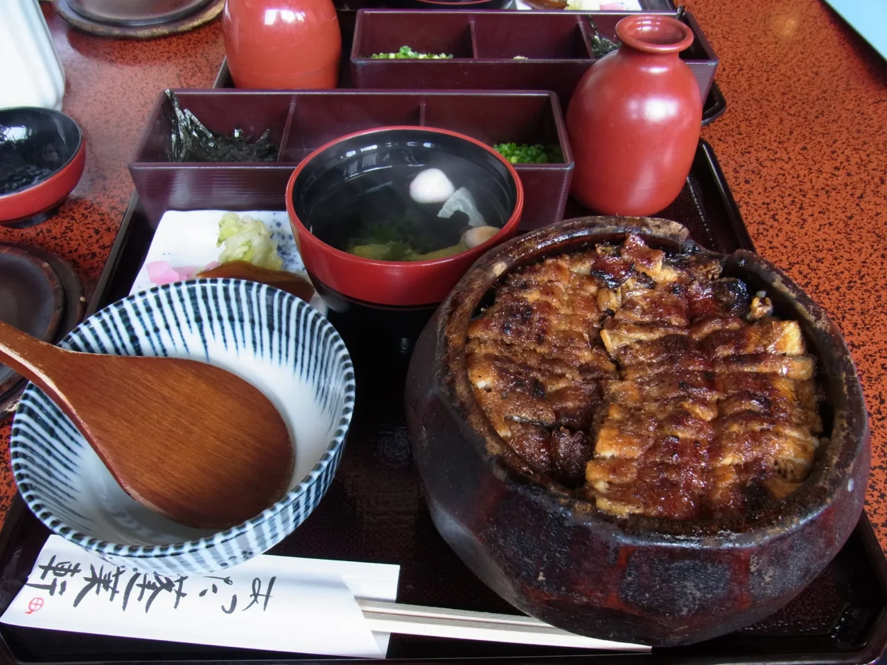 黑铁锅盛装格纹烤穴子，配白瓷碗芋类、红漆杯及黑漆碗的日式套餐组合。