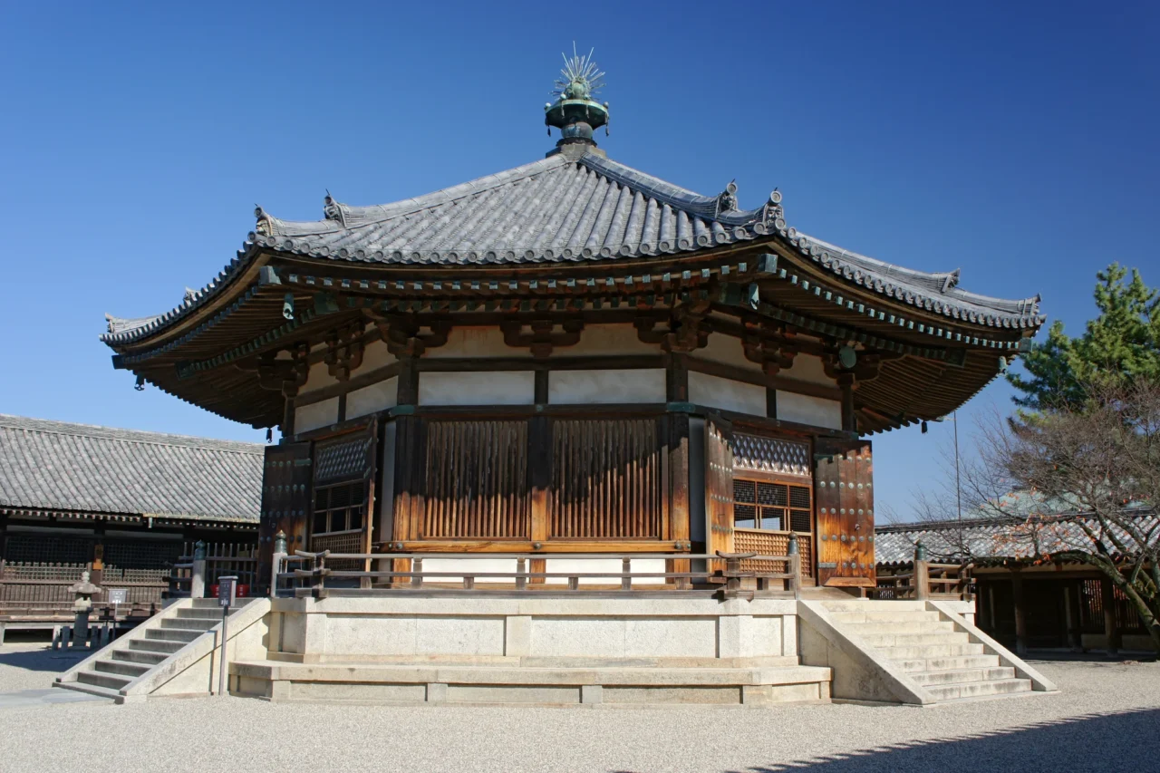 八角形木造寺院堂宇，棕色木門、灰瓦屋頂，石階平台前排列，晴天蒼空下白砾石地面。