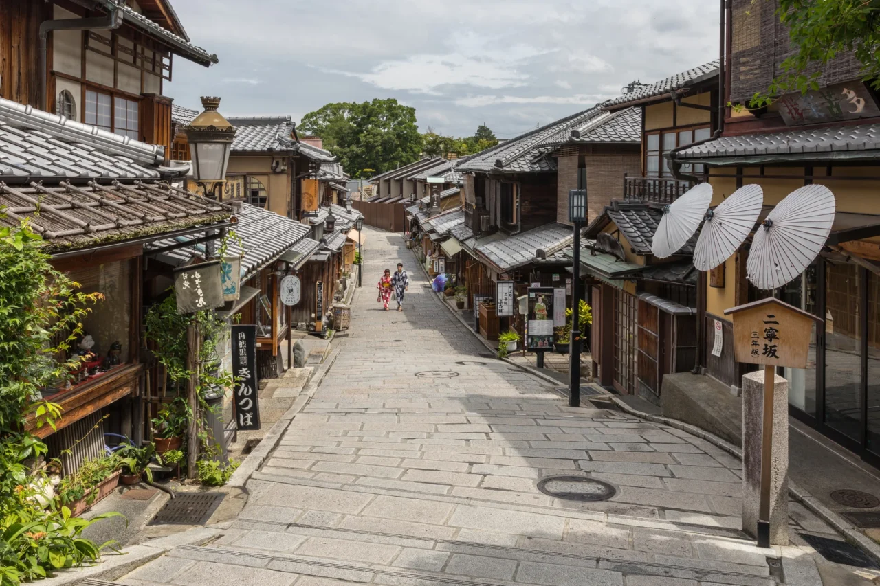 传统木造建筑两侧的石板街道，白色圆形灯笼装饰店铺入口，阴天白光下行人散落远处。