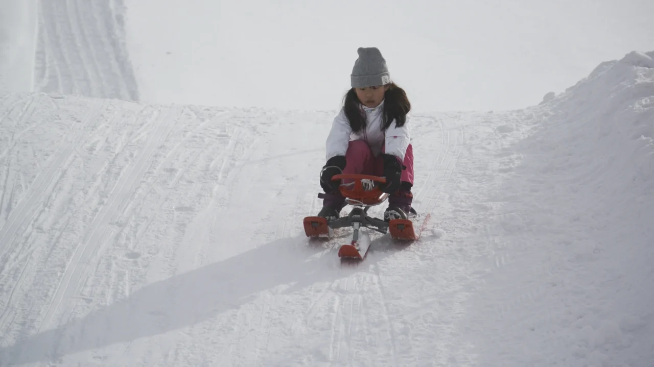 女性穿冬裝坐紅色雪橇在白雪山坡滑行,陰沉天氣、能見度低的冬季場景。