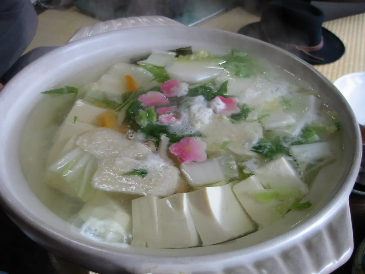 白瓷碗盛清湯豆腐,白菜及粉紅黃花瓣點綴,室内用餐場景。