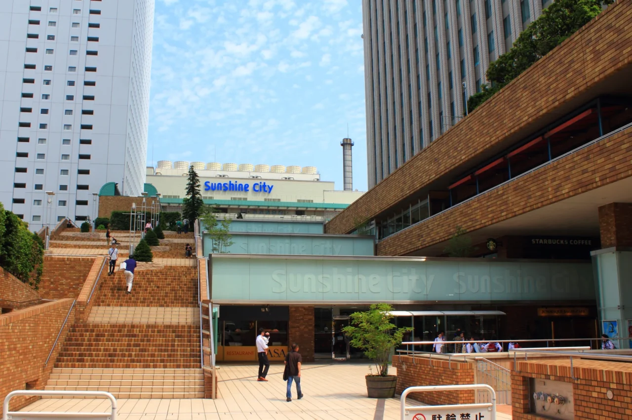 淡綠色招牌的 Landmark City 建築入口,紅磚廣場上幾位行人,晴朗藍天與現代玻璃建築背景。