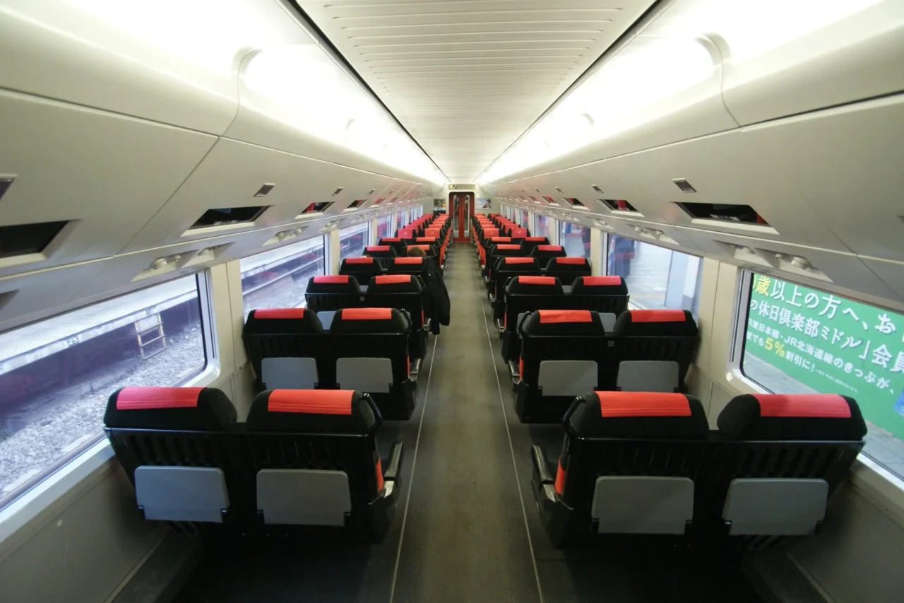 Skyliner快線列車車廂,白天日光穿透車窗,兩排紅色座墊黑色座椅整齊排列,天花板潔白。