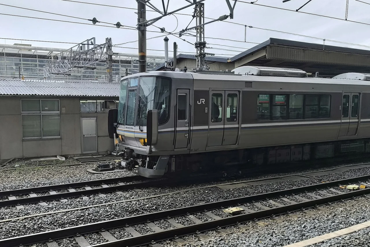 JR銀灰色近郊列車停靠京都站月台,車頭亮著黃色頭燈,上方為月台雨棚。