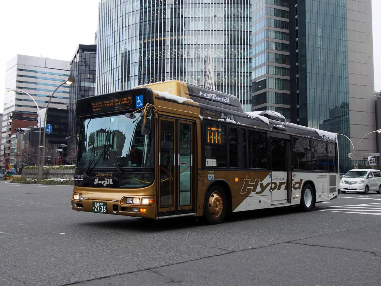 金色塗裝的 Me~guru 觀光巴士行駛於名古屋市中心街頭，車頭與車側可見メーグル字樣。
