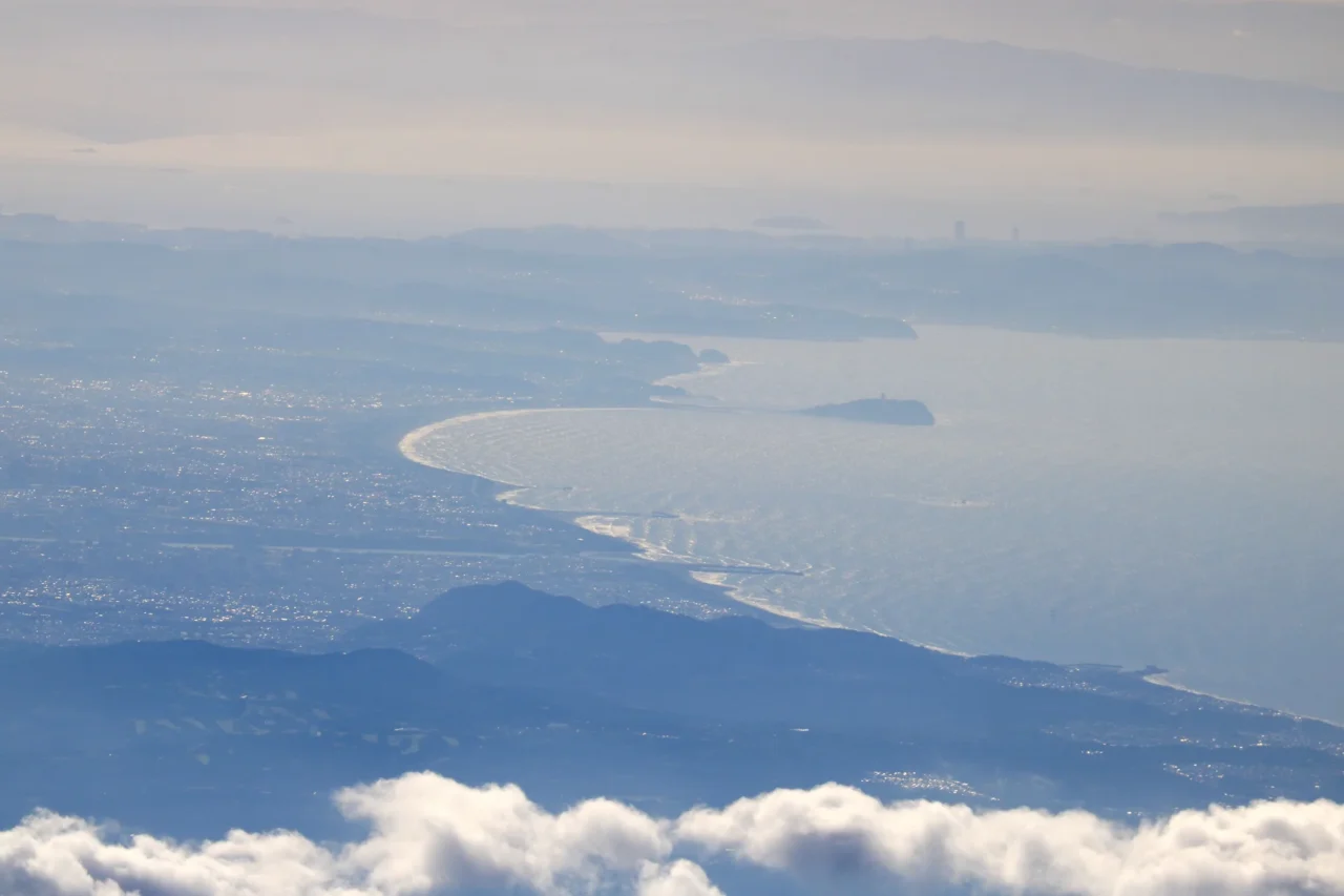 江之島與湘南海岸海景，白天陽光下海岸線清晰，遠景青山與近景沙灘構成寧靜海灘景觀。