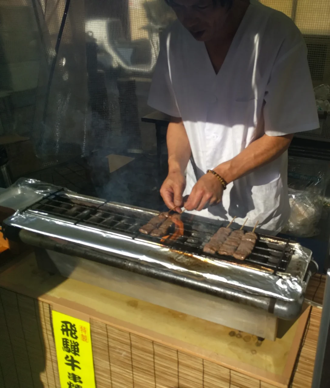 櫻山八幡宮飛騨牛烤肉，室內木臺上白襯衫職員操作金屬烤架，黃色標牌標示。