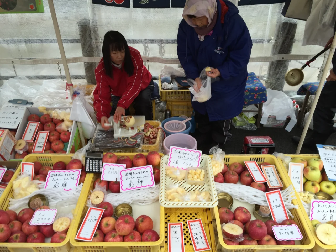 宮川朝市新鮮水果攤位，玻璃棚遮蔽下擺放帶標籤的蘋果、草莓、番茄。