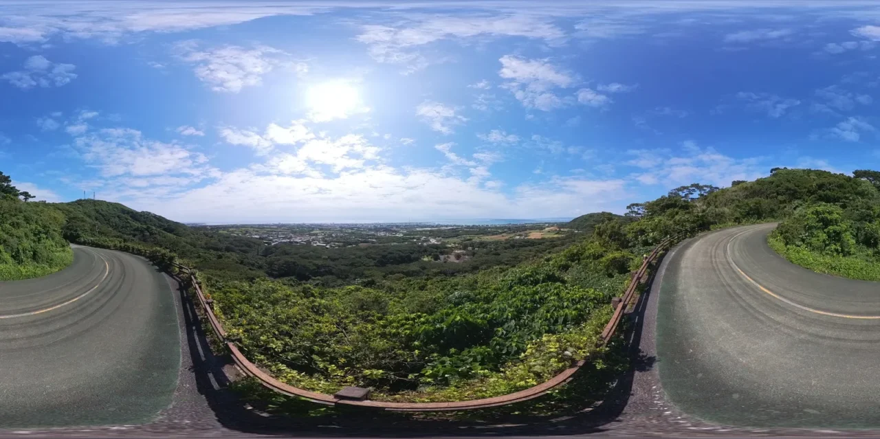 石垣島自駕環島路線，彎曲山路景觀，樹林地帶與平原遠景，晴日拍攝。