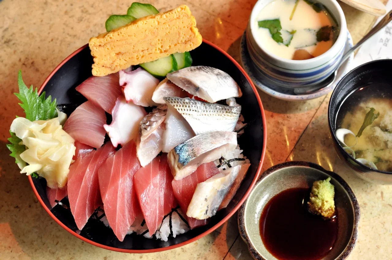 紅黑圓盤的海鮮丼,盛裝鮪魚、貝類、蛋卷與調料,展現市場食堂特色。