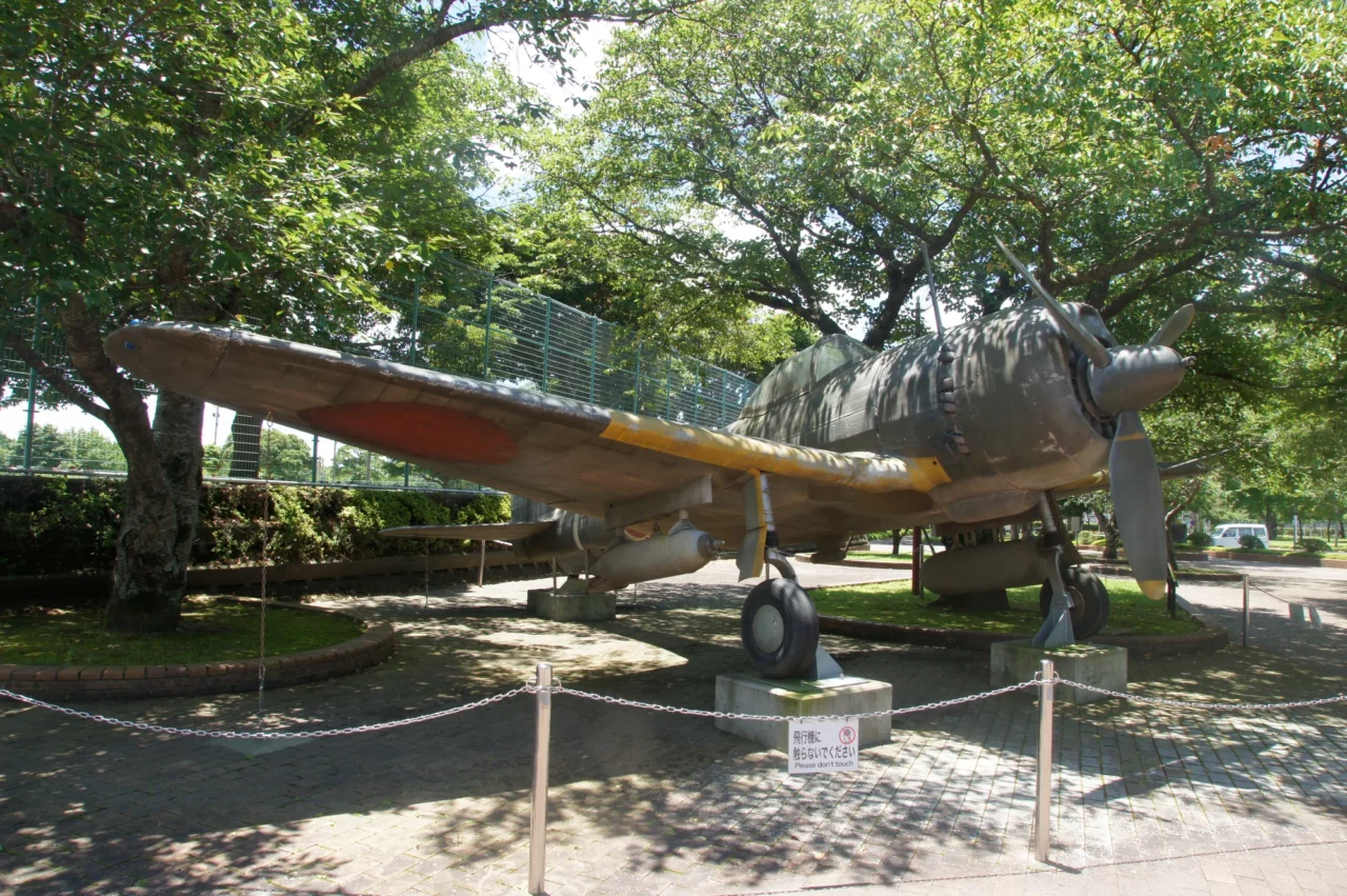 知覧特攻平和會館戶外展場停放的棕褐色單引擎軍用飛機,四周環繞高大樹木