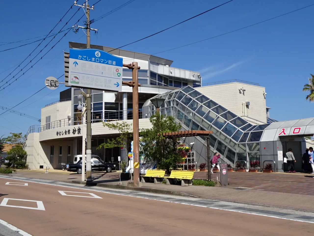 开闻岳映衬指宿砂蒸温泉海滨，黑色火山砂闪烁阳光，游客浸浴天然地热中。