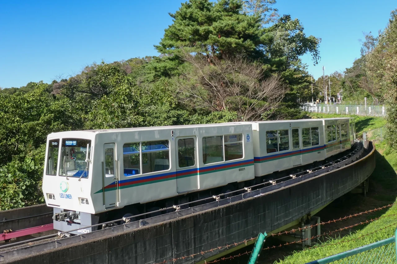 西武園遊樂園綠白色電車停靠於林間軌道，晴朗藍天襯託郊外田園風景
